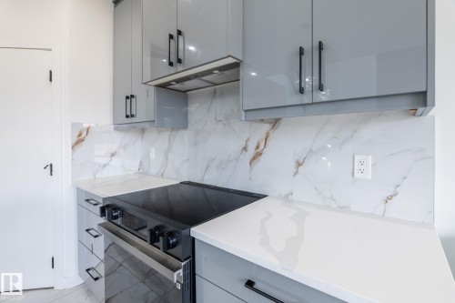 Sleek kitchen featuring light gray high-gloss cabinetry with matte black pulls, white countertops, and a white backsplash with gold veining - 6607 50A Avenue, Beaumont, AB - Indoor Photo Showing Kitchen