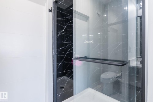 Glass-enclosed shower with black-veined wall tiling, black frame, and a dark handle - 6607 50A Avenue, Beaumont, AB - Indoor Photo Showing Bathroom