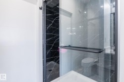 Glass-enclosed shower with black-veined wall tiling, black frame, and a dark handle - 