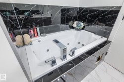 Corner jetted soaking tub featuring chrome fixtures set against black marble-patterned tile, with white wall and floor tiles - 