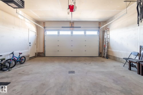 Two-car garage featuring a paneled automatic door with upper light panels, concrete flooring, and an interior access door - 6607 50A Avenue, Beaumont, AB - Indoor Photo Showing Garage