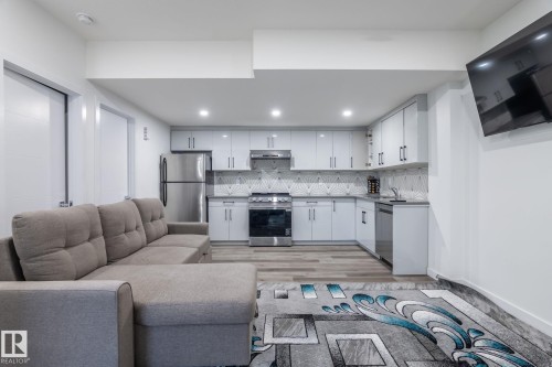 Modern kitchen featuring white cabinetry, stainless steel appliances, and a geometric tile backsplash - 6607 50A Avenue, Beaumont, AB - Indoor