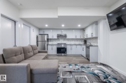 Open-concept living space featuring a modern kitchen with white cabinetry, stainless steel appliances, and geometric backsplash - 