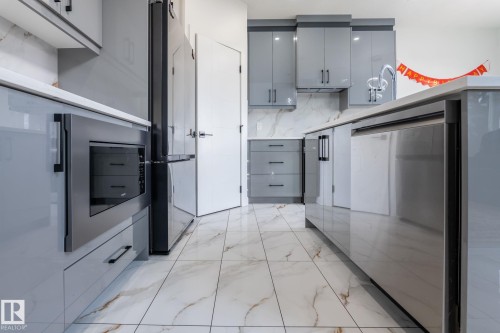 Modern kitchen featuring white tile flooring with brown veining, light gray cabinetry, built-in stainless steel microwave, and integrated stainless steel dishwasher - 6607 50A Avenue, Beaumont, AB - Indoor Photo Showing Kitchen