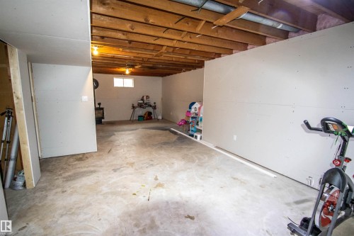 Unfinished basement space featuring exposed wood joists and subflooring, partial drywall installation, and a concrete floor - 5125 46 Ave, St. Paul Town, AB - Indoor