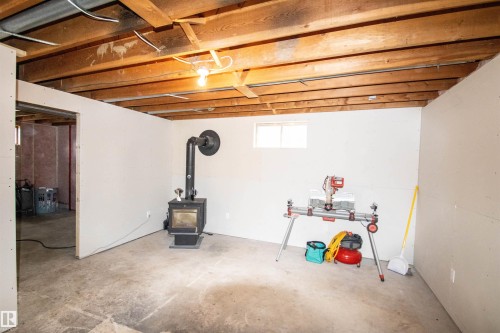 Partially finished lower level featuring exposed wood beam ceiling, concrete flooring, and a free-standing stove - 5125 46 Ave, St. Paul Town, AB - Indoor Photo Showing Basement