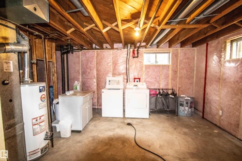 Unfinished basement space featuring exposed wooden beams, concrete flooring, a laundry area with two appliances, and a utility sink with white cabinetry - 5125 46 Ave, St. Paul Town, AB - Indoor Photo Showing Basement