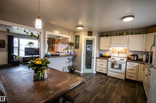 Expansive kitchen featuring wood-finish flooring, white cabinetry, dark countertops, and a full suite of white appliances - 5125 46 Ave, St. Paul Town, AB - Indoor