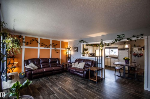 Spacious living area featuring wood-finish flooring, a decorative accent wall with vertical and horizontal trim, and an open pass-through to the kitchen - 5125 46 Ave, St. Paul Town, AB - Indoor Photo Showing Living Room