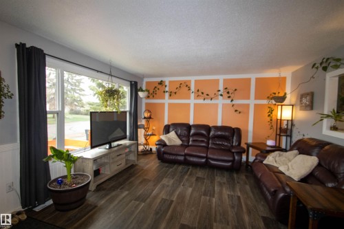 Spacious living area featuring wood-finish flooring, a large picture window, a decorative accent wall, and a textured ceiling - 5125 46 Ave, St. Paul Town, AB - Indoor Photo Showing Living Room