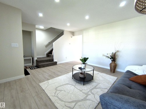 Open-concept living space with light wood-finish flooring, recessed lighting, and a staircase featuring carpeted treads and a white handrail - 14125 30 Street, Edmonton, AB - Indoor