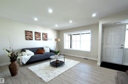 Bright living area featuring wood-finish flooring, recessed ceiling lighting, a large picture window, and a paneled entry door with sidelight - 