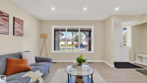 Spacious living area featuring light wood-finish flooring, recessed lighting, and a large front-facing window with white trim - 14125 30 Street, Edmonton, AB - Indoor