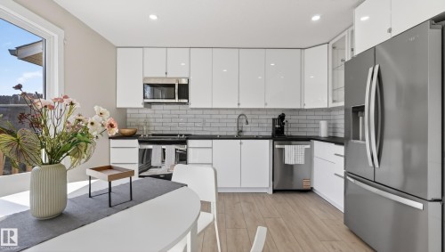 Modern kitchen featuring white gloss cabinetry, subway tile backsplash, dark countertops, and stainless steel appliances - 14125 30 Street, Edmonton, AB - Indoor Photo Showing Kitchen With Upgraded Kitchen