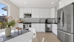 Modern kitchen featuring white gloss cabinetry, subway tile backsplash, dark countertops, and stainless steel appliances - 