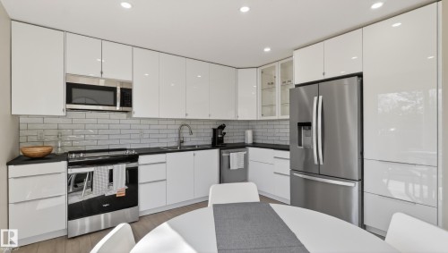 Contemporary kitchen with glossy white cabinetry, stainless steel appliances, black countertops, and subway tile backsplash - 14125 30 Street, Edmonton, AB - Indoor Photo Showing Kitchen With Double Sink With Upgraded Kitchen