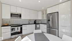 Contemporary kitchen with glossy white cabinetry, stainless steel appliances, black countertops, and subway tile backsplash - 
