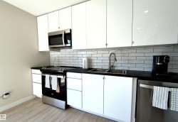 Modern kitchen featuring white cabinetry, dark countertops, a subway tile backsplash, stainless steel appliances, and wood-finish flooring - 