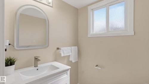 White vanity with an integrated sink and brushed nickel faucet, illuminated by an arched mirror with integrated lighting - 14125 30 Street, Edmonton, AB - Indoor Photo Showing Bathroom