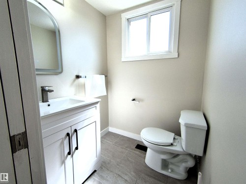 Bathroom featuring a white vanity with black hardware, a rectangular sink, a contemporary faucet, an arched mirror, and a window - 14125 30 Street, Edmonton, AB - Indoor Photo Showing Bathroom