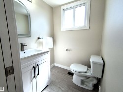 Bathroom featuring a white vanity with black hardware, a rectangular sink, a contemporary faucet, an arched mirror, and a window - 