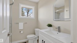 Full bathroom featuring a single white vanity with an integrated sink, a contemporary mirror, a toilet, a window, and a glass-enclosed shower - 