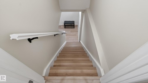 Staircase with light wood-finish treads and risers, white baseboards, and a white wall-mounted handrail with black brackets - 14125 30 Street, Edmonton, AB - Indoor Photo Showing Other Room