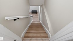 Staircase with light wood-finish treads and risers, white baseboards, and a white wall-mounted handrail with black brackets - 