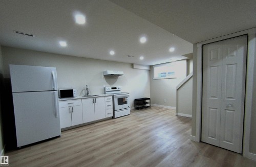 Kitchen area featuring white cabinetry, a compact appliance suite, wood-finish flooring, recessed lighting, and a bi-fold closet - 14125 30 Street, Edmonton, AB - Indoor