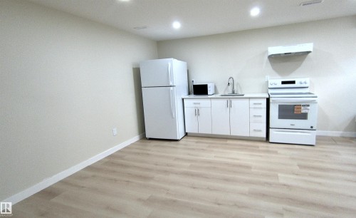 Contemporary kitchen featuring white cabinetry, a stainless steel sink, and light wood-finish flooring - 14125 30 Street, Edmonton, AB - Indoor
