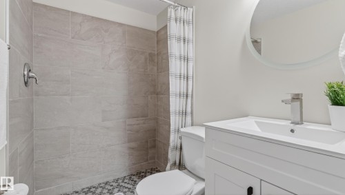 Bathroom featuring a white vanity with an integrated sink, brushed nickel faucet, large circular mirror, and tiled shower with mosaic flooring - 14125 30 Street, Edmonton, AB - Indoor Photo Showing Bathroom