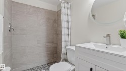 Bathroom featuring a white vanity with an integrated sink, brushed nickel faucet, large circular mirror, and tiled shower with mosaic flooring - 