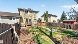 Expansive backyard featuring a manicured lawn area, wood chip landscaping, and a privacy fence - 