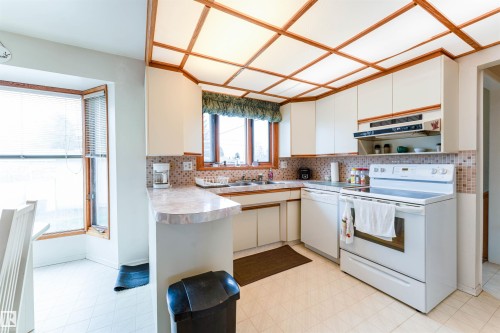 Kitchen featuring white cabinetry, white appliances, a patterned tile backsplash, and a drop ceiling with wood-finish trim - 13231 74 Street, Edmonton, AB - Indoor