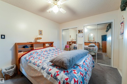 Carpeted room featuring a ceiling fan with integrated lighting, wood-finish headboard with built-in shelving, and two sliding mirror closet doors - 13231 74 Street, Edmonton, AB - Indoor Photo Showing Bedroom