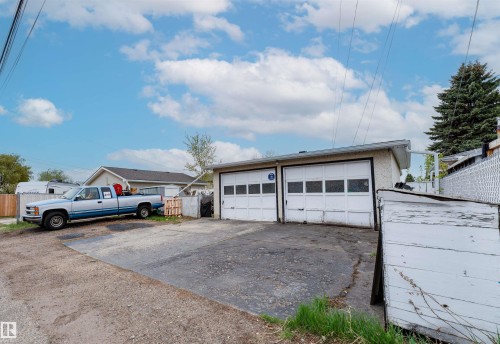 Detached garage structure featuring two overhead doors, a stucco exterior, and a gravel/asphalt driveway - 13231 74 Street, Edmonton, AB - Outdoor