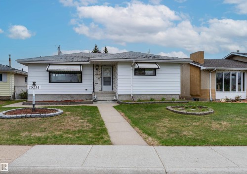 White siding exterior with a dark gray shingle roof, concrete front walkway, and two front yard garden beds with decorative edging - 13231 74 Street, Edmonton, AB - Outdoor