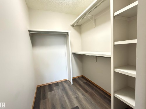 Walk-in closet featuring wood-finish flooring, white walls, built-in shelving, and multiple hanging rods - 309 10610 76 Street, Edmonton, AB - Indoor With Storage