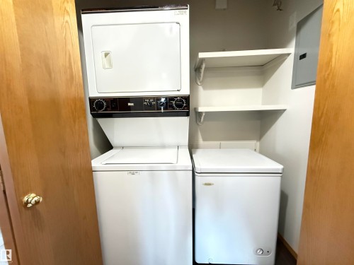 Dedicated utility closet featuring a stacked washer and dryer, additional chest freezer, and two white shelving units - 309 10610 76 Street, Edmonton, AB - Indoor Photo Showing Laundry Room