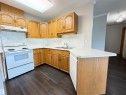 Kitchen featuring wood-finish cabinetry, white countertops, a stainless steel sink, and white appliances - 309 10610 76 Street, Edmonton, AB  - Indoor Photo Showing Kitchen With Double Sink 