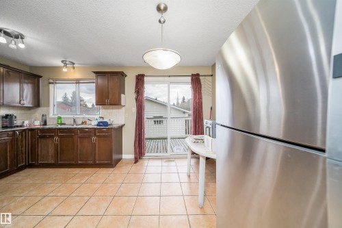 Kitchen featuring warm-toned floor tiles, dark wood cabinetry, and a stainless steel refrigerator - 1771 37 Street, Edmonton, AB - Indoor Photo Showing Kitchen With Double Sink