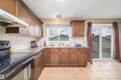 Kitchen featuring wood-finish cabinetry, tile flooring, and a sliding glass door leading to an outdoor deck - 1771 37 Street, Edmonton, AB - Indoor Photo Showing Kitchen With Double Sink
