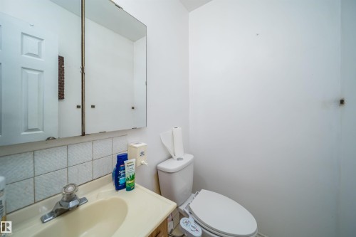 Bathroom featuring a white toilet, wall-mounted medicine cabinet, and a single-handle faucet over a drop-in sink with a tiled backsplash - 1771 37 Street, Edmonton, AB - Indoor Photo Showing Bathroom