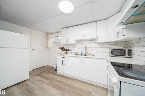 Kitchen featuring white cabinetry, light-toned countertops, a subway tile backsplash, and wood-finish flooring - 1771 37 Street, Edmonton, AB - Indoor Photo Showing Kitchen
