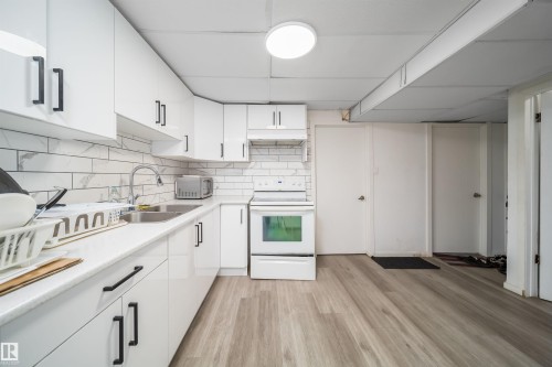 Kitchen featuring white cabinetry with black hardware, white subway tile backsplash, stainless steel double basin sink, and wood-finish flooring - 1771 37 Street, Edmonton, AB - Indoor Photo Showing Kitchen With Double Sink