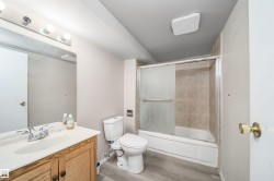 Bathroom featuring a vanity with a white countertop and wood-finish cabinetry, a toilet, and a tub with a sliding glass enclosure and tiled surround - 