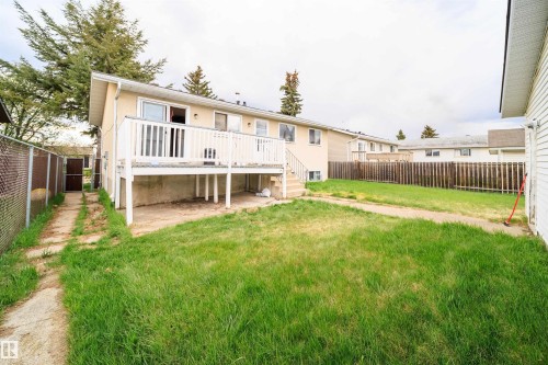 Expansive backyard featuring a raised wooden deck with white railing, a concrete patio area below the deck, a chain-link fence bordering a side pathway, and a wooden privacy fence at the property's rear - 1771 37 Street, Edmonton, AB - Outdoor With Deck Patio Veranda