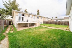 Expansive backyard featuring a raised wooden deck with white railing, a concrete patio area below the deck, a chain-link fence bordering a side pathway, and a wooden privacy fence at the property's rear - 