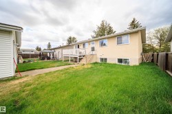 Expansive rear yard featuring a grass lawn, a wood deck with white railings, and a concrete pathway - 