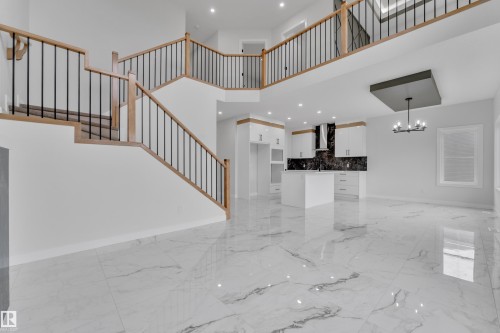 Open-concept interior featuring a grand staircase with wood railings and black spindles, large format marble-look tile flooring, and a modern kitchen with white cabinetry and dark stone backsplash - 12623 44 Street, Edmonton, AB 